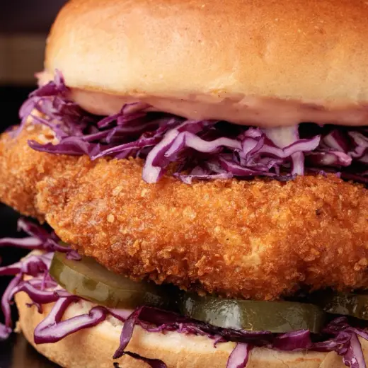 Close-up of a crunchy chicken fillet with purple slaw and pickles